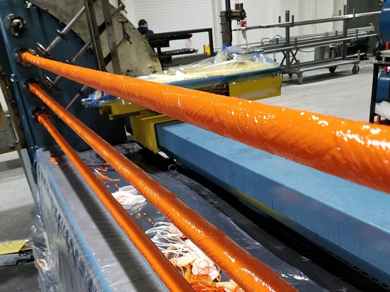 Factory interior with filament winding machinery. Wet, orange fiberglass tow is being wound onto a mandrel.